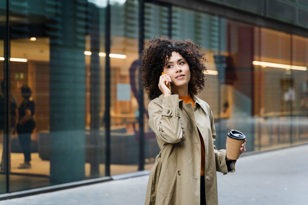 vrouw met koffie en telefoon buiten gebouw